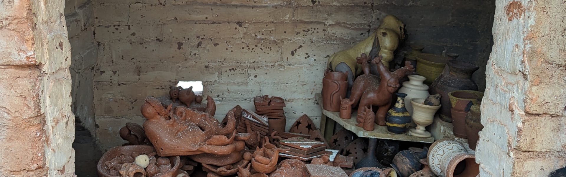 Looking through the open door of a brick kiln, we see ceramic vases, bowls, and dishes piled on top of each other with a thin layer of ash coating everything.